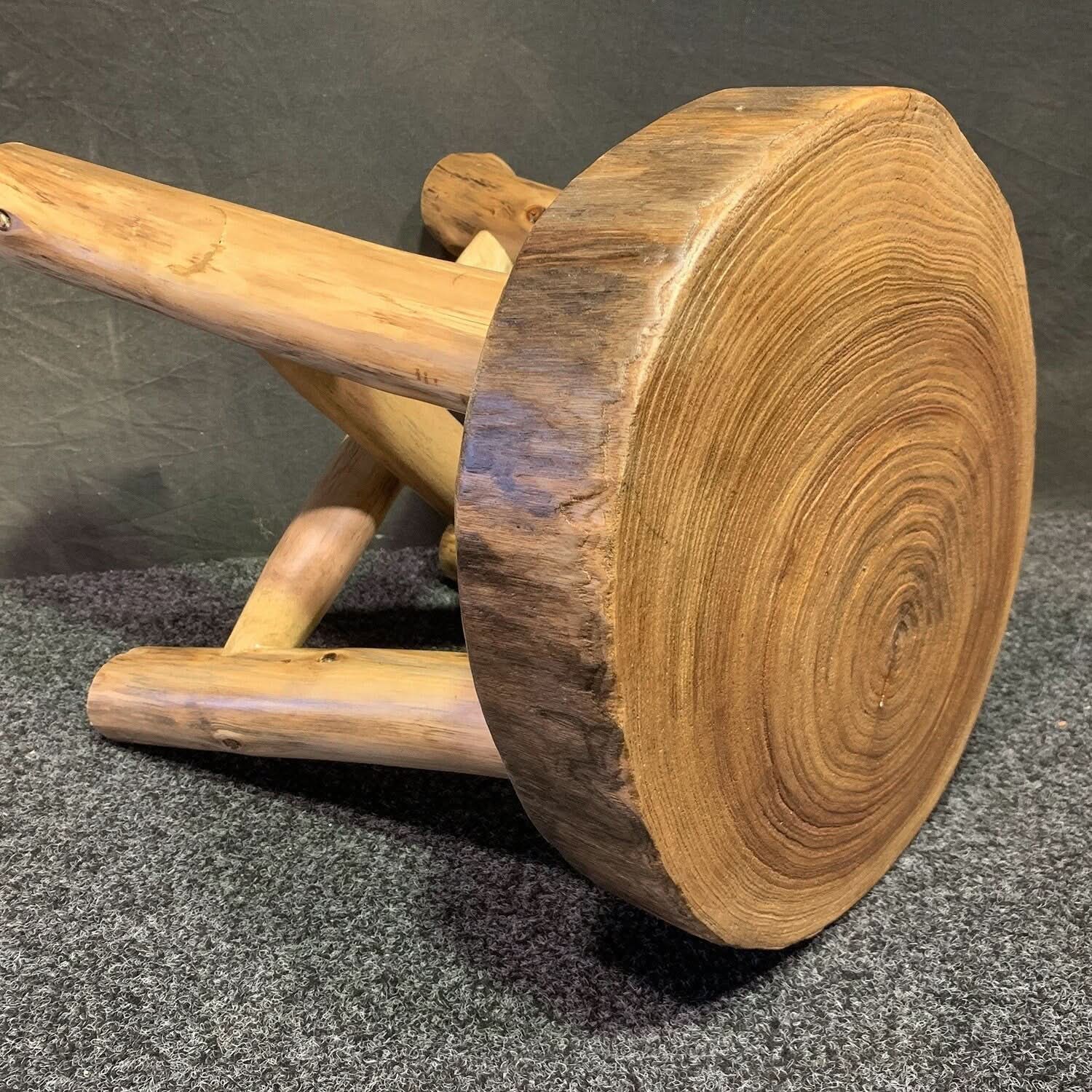 Solid wood tree ring stool with natural wood grain and rustic legs on grey carpet.