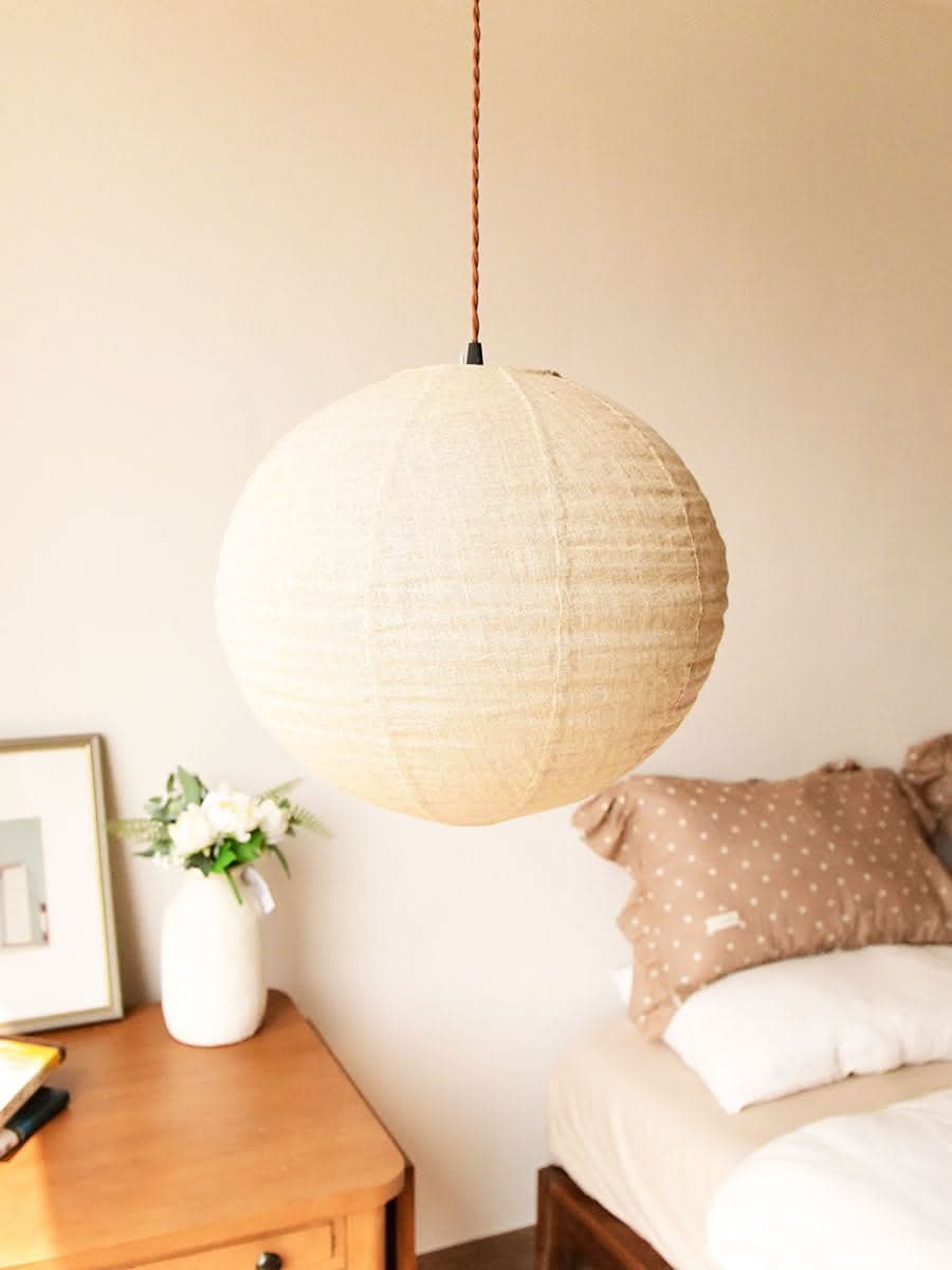 Natural linen ceiling shade, round, hangs in a cozy bedroom with pillows and bedside table.