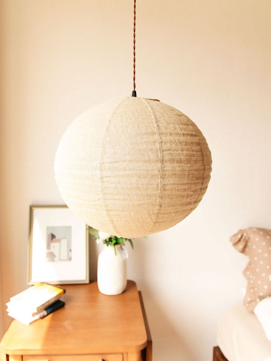 Natural linen ceiling shade, round shape, hanging above a wooden nightstand with decor.