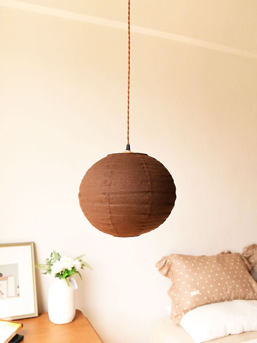 Round Linen Ceiling Shade in warm brown, hanging above a bedside table with decor.