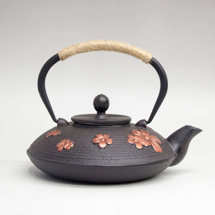 Dark iron tea kettle with copper cherry blossom accents and natural rope handle.