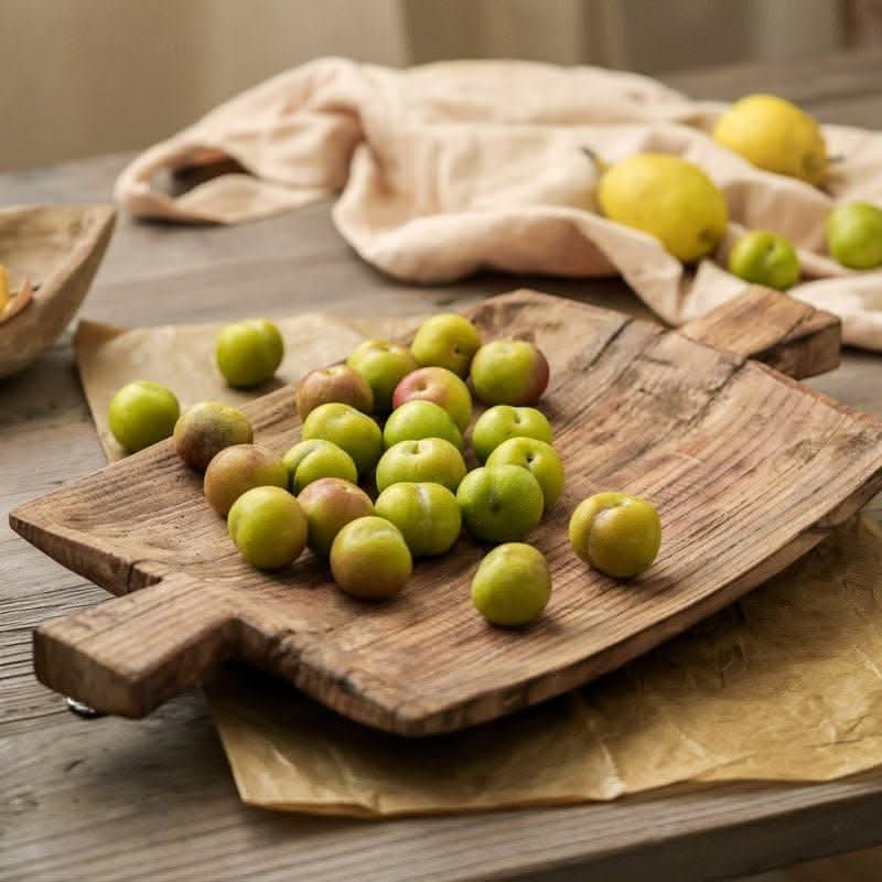 Irregular rectangular wooden serving tray with green plums and lemons on a rustic table.