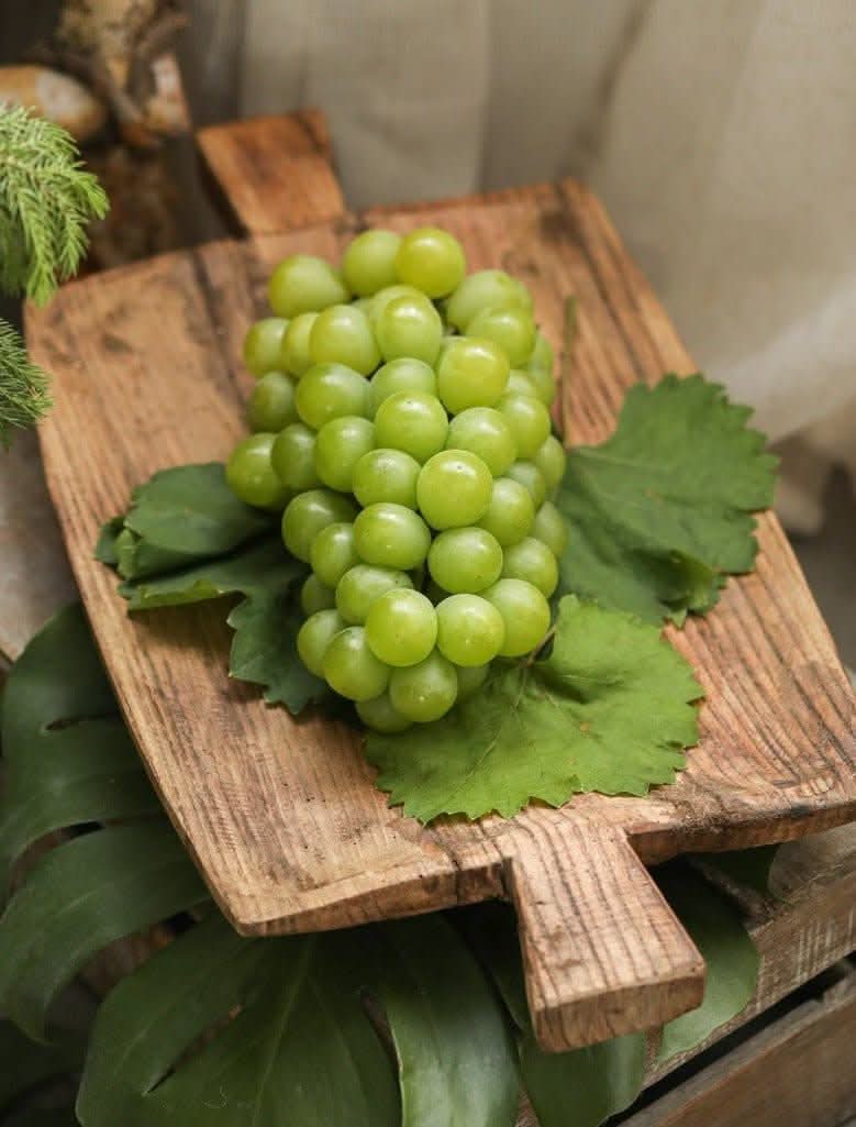 Irregular rectangular wooden serving tray with green grapes and leaves.
