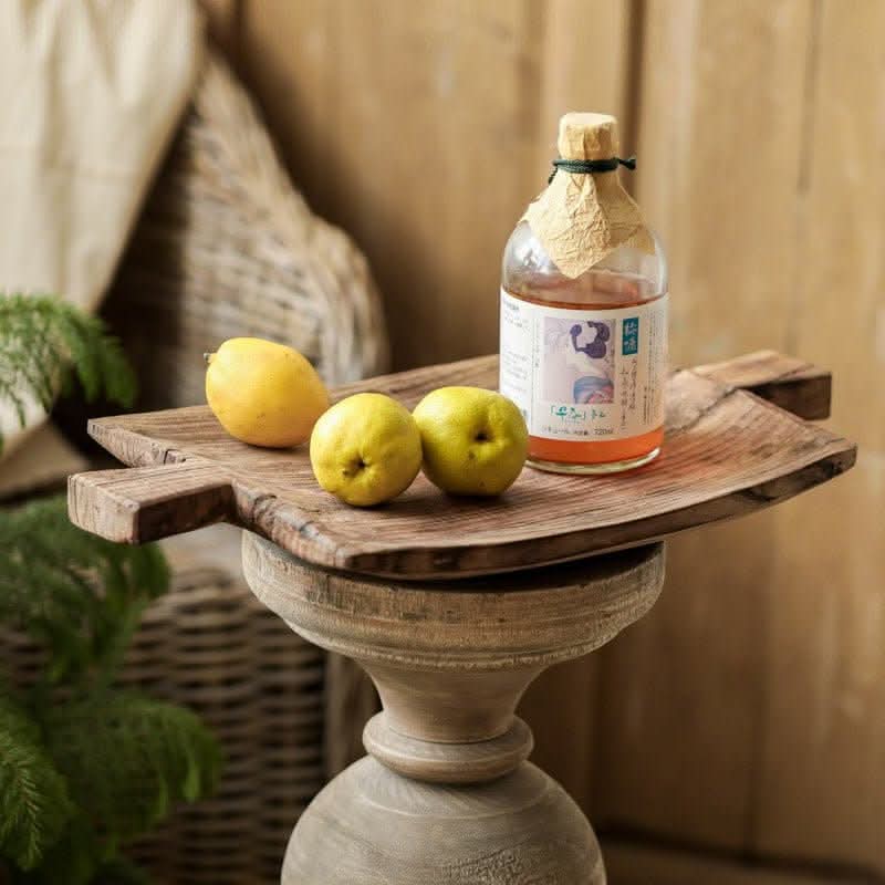 Rustic irregular rectangular wooden serving tray with lemons and bottle on pedestal.