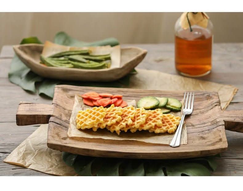 Irregular rectangular wooden serving tray with waffles and sliced vegetables.