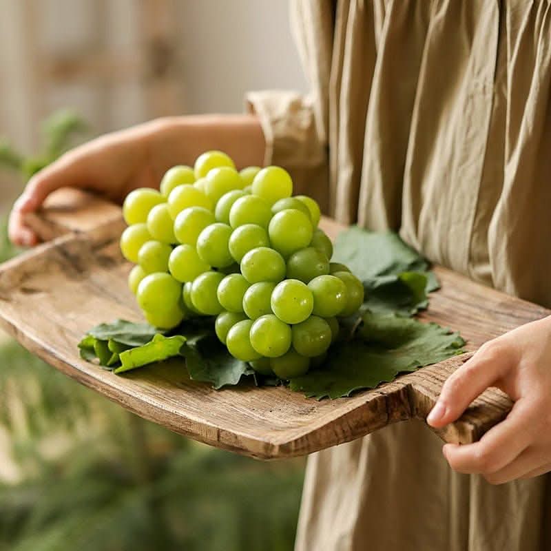 Irregular rectangular wooden serving tray with green grapes and leaves, natural wood finish.