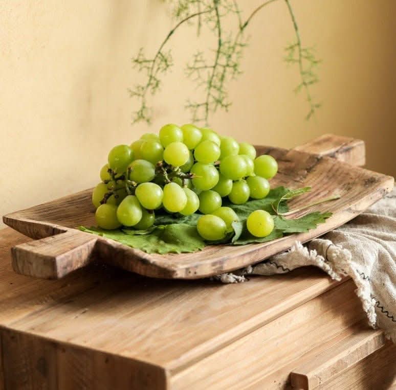 Rustic irregular rectangular wooden serving tray with green grapes on a neutral background.