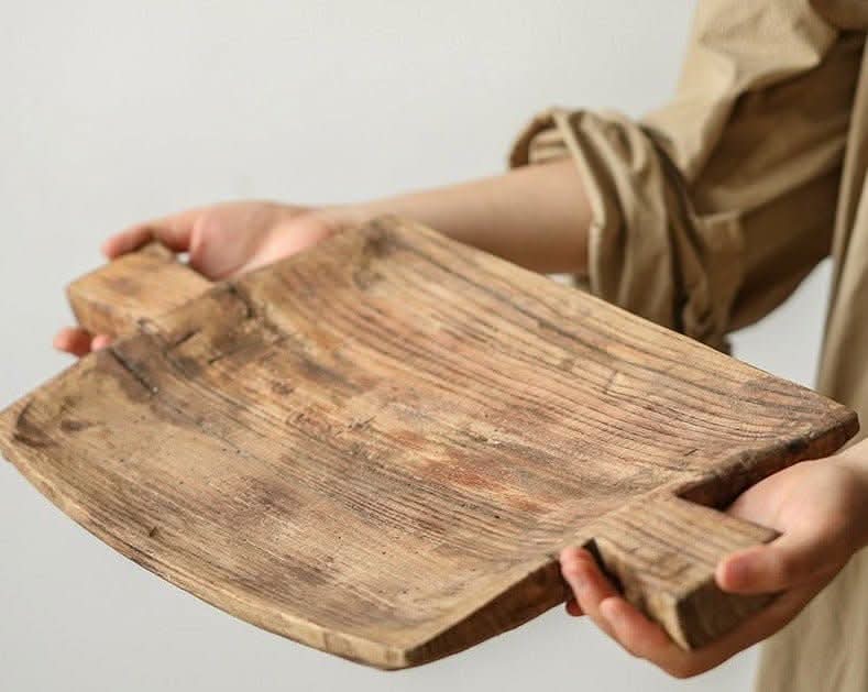 Rustic irregular rectangular wooden serving tray with handles, held by hands.