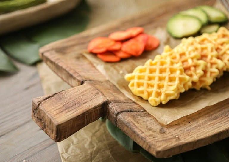 Rustic irregular rectangular wooden serving tray with waffles, orange slices, and cucumber slices.