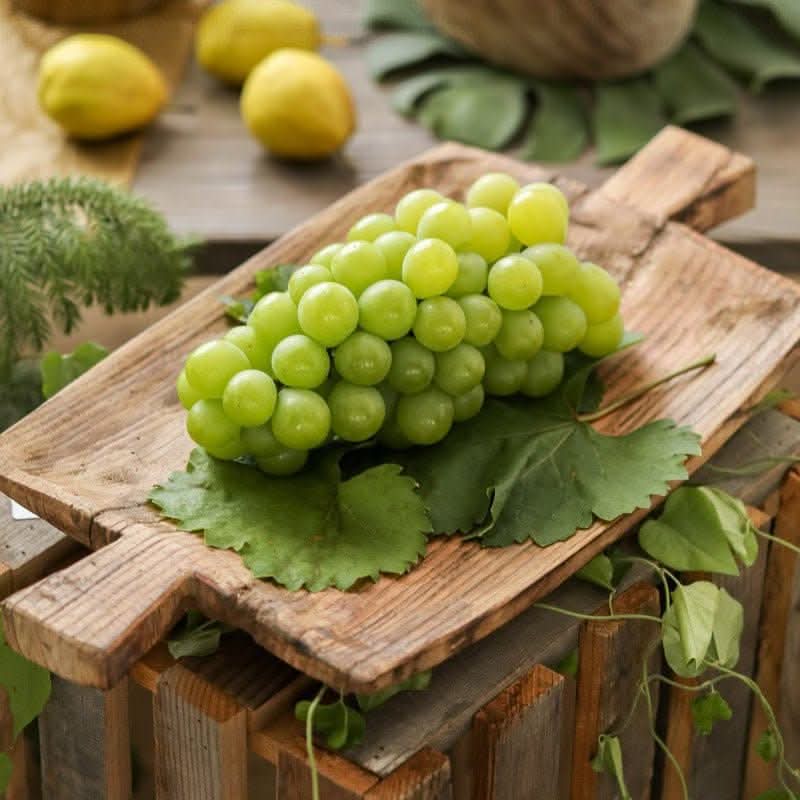 Irregular rectangular wooden serving tray with green grapes and leaves on a rustic surface.