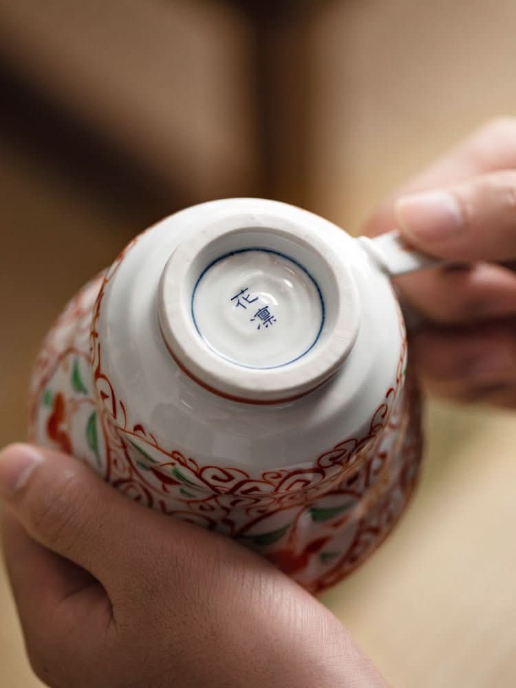 Hands hold Japan Imported Bloom Red-painted Cherry Branch Mug with red, green, and white floral design.