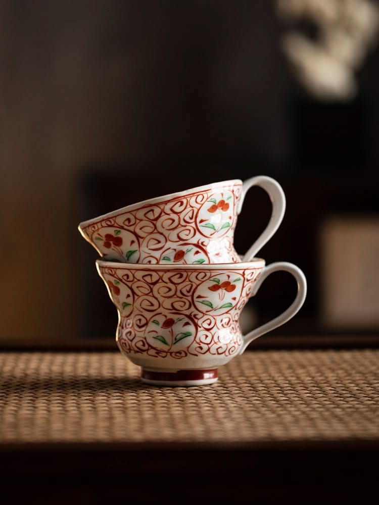 Japan Imported Bloom Red-painted Cherry Branch Mug stacked on a woven mat, with intricate red and green floral design.