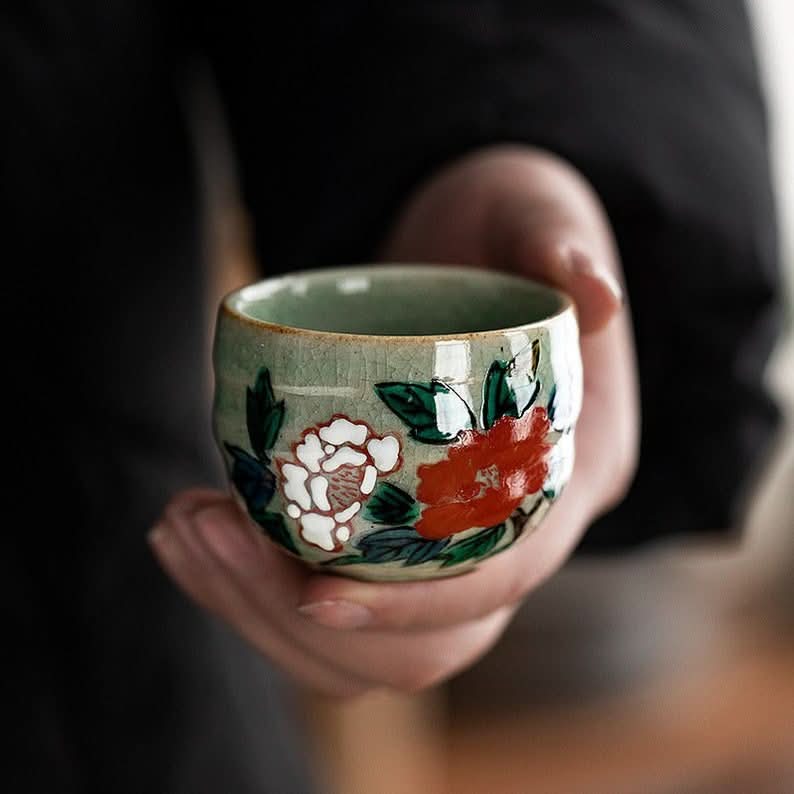 Green ceramic Five-Herb Flower Tea Cup Set with red and white floral design, held in hands.