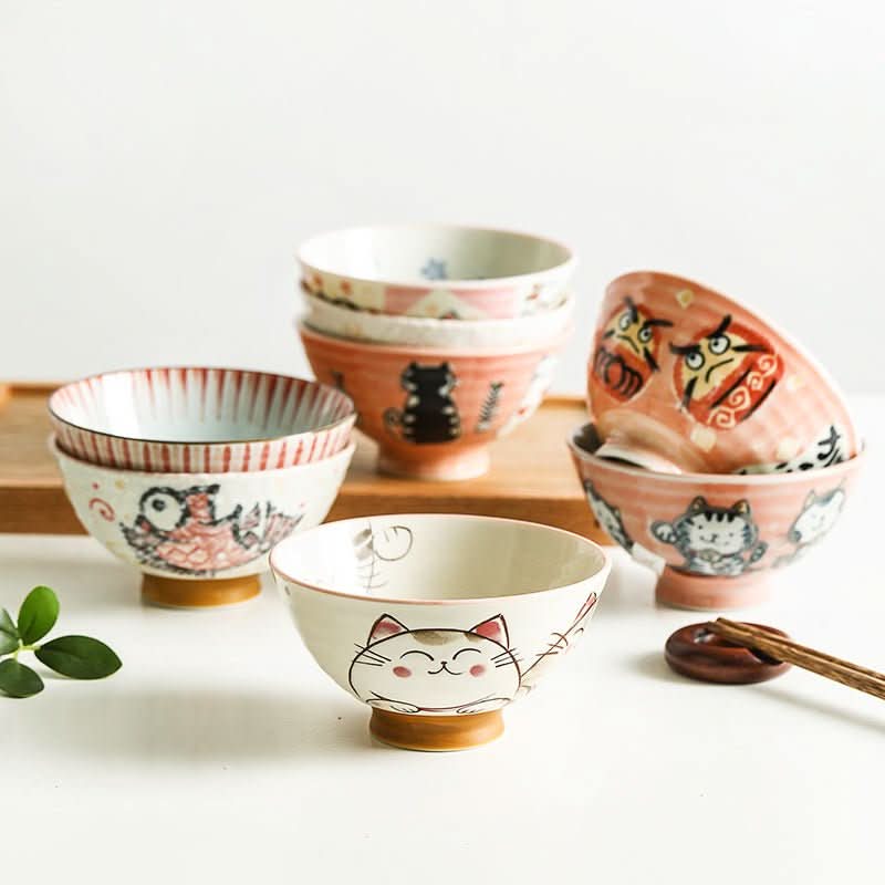 Japanese bowls with illustrations of cats and Daruma dolls in ceramic on a wooden tray.