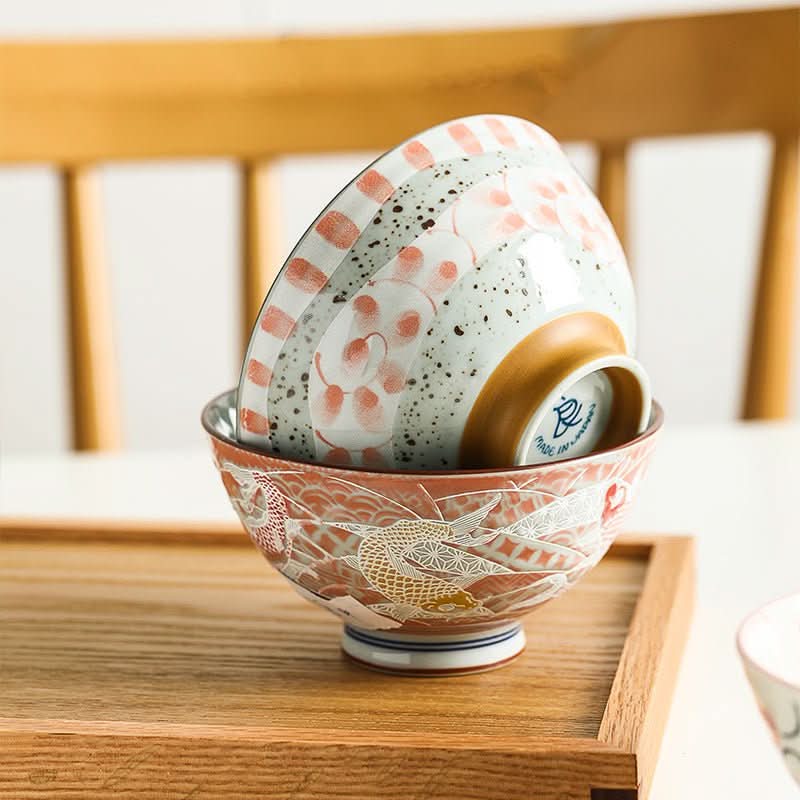 Stack of Japanese bowls with intricate fish and floral illustrations in red, white, and speckled gray.