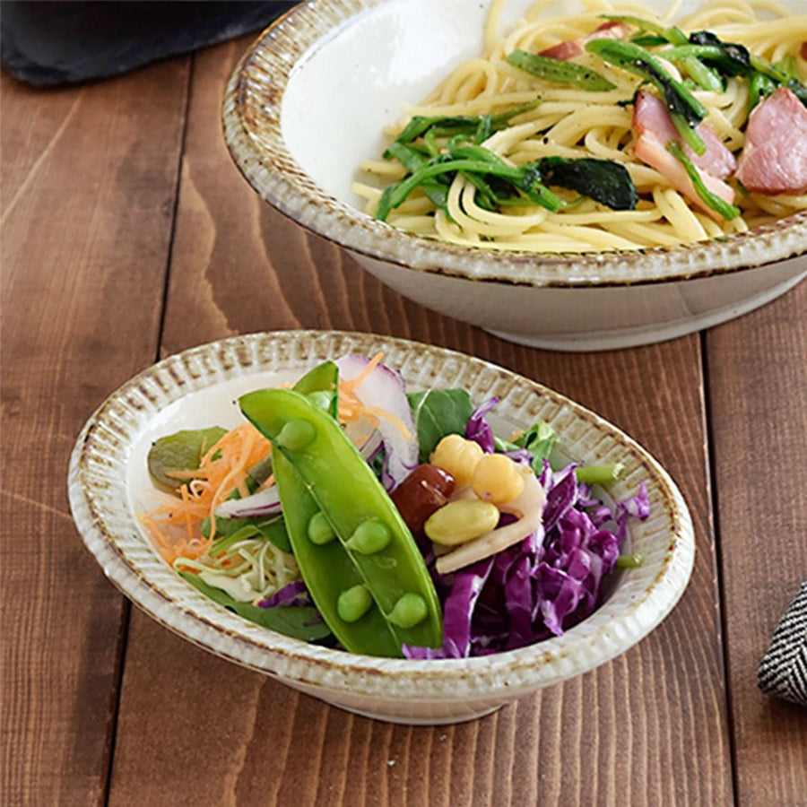 Japan imported Mino Ware beige stoneware dishes with pasta and salad on rustic wood table.