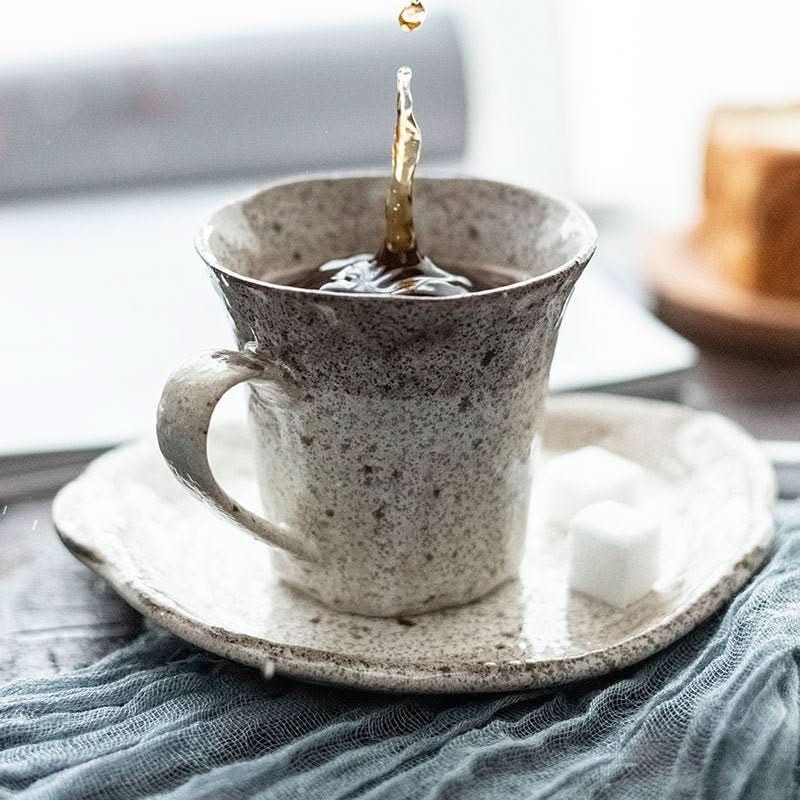 Japan Imported Mino Yaki Tea Powder Lead Set Cup with a splash of liquid, on a textured saucer with sugar cubes.