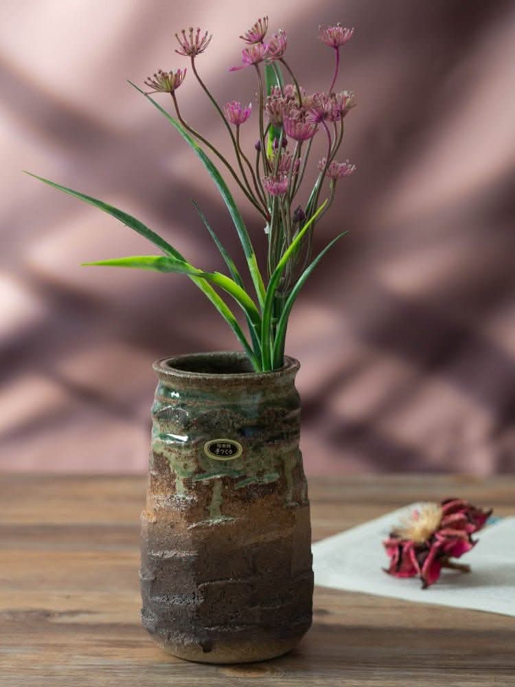 Japan imported stoneware pottery vase with green & brown glaze, holding pink wildflowers.