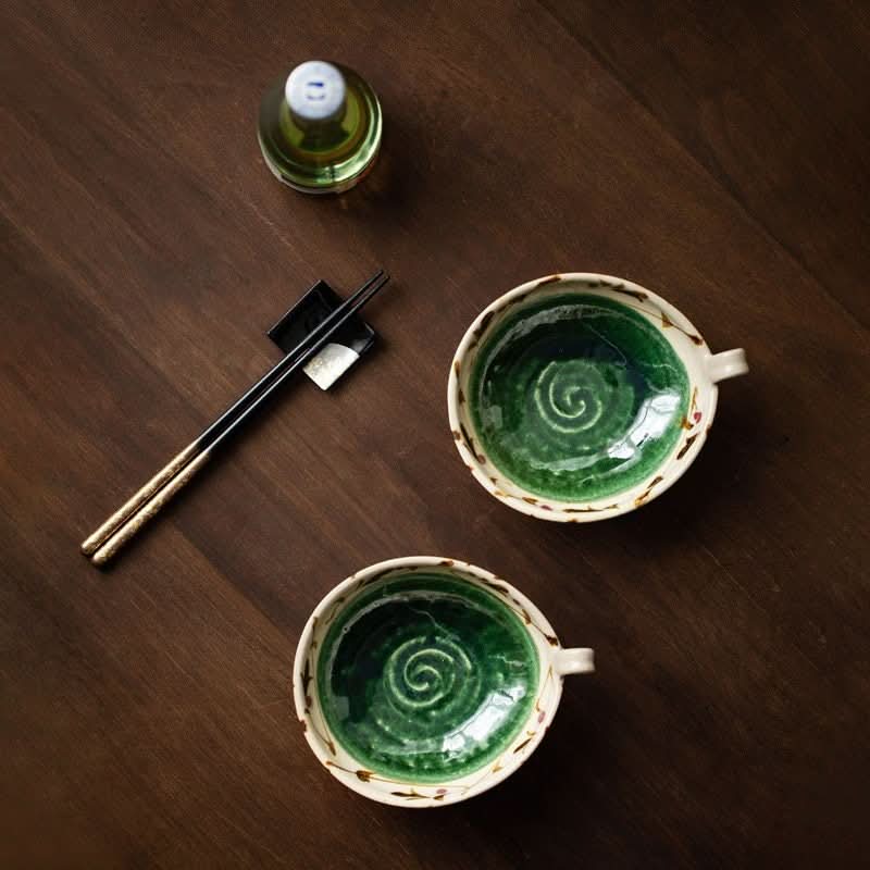 Two green Japanese ceramic bowls with handles and spiral pattern, on a wooden table.