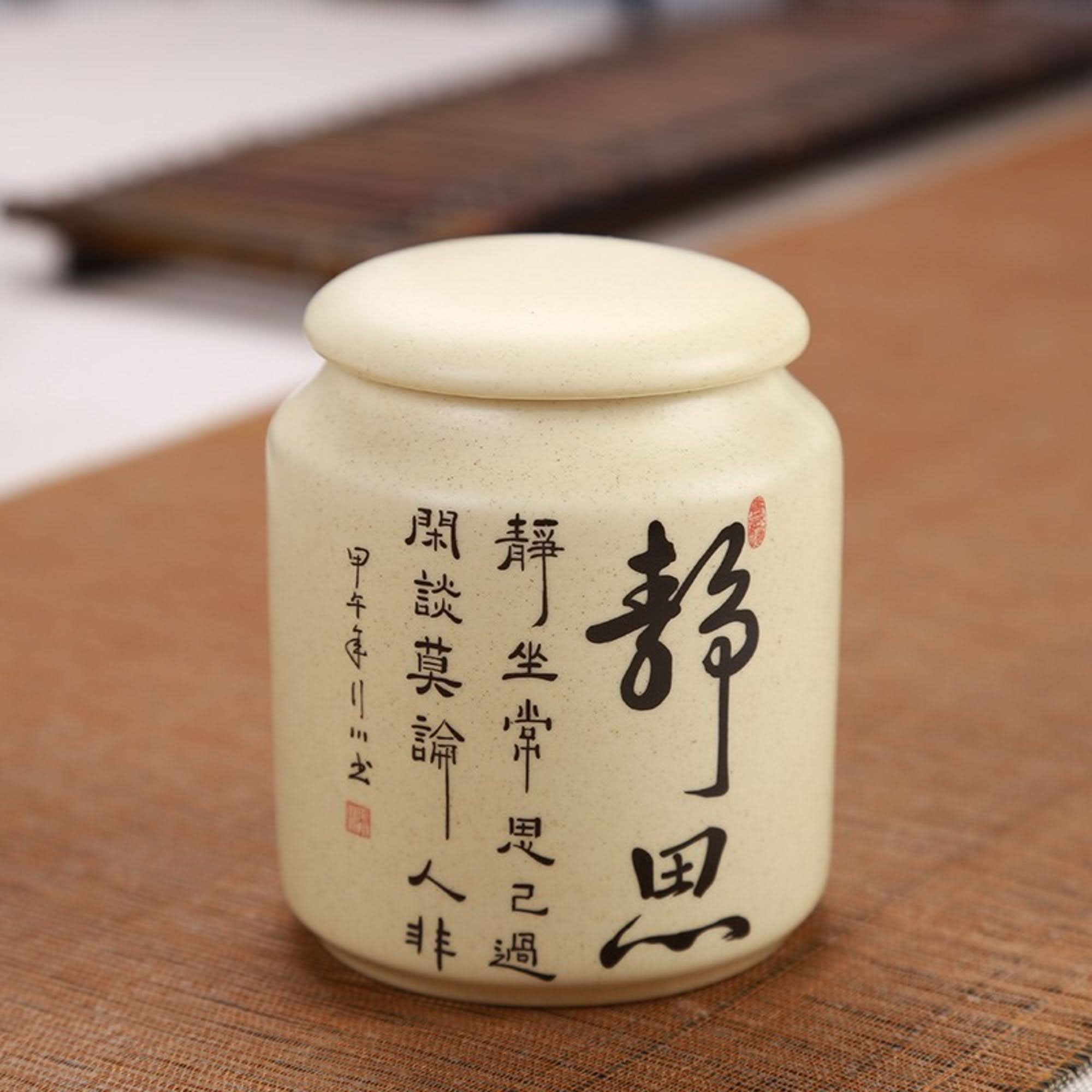 Japanese art ceramic tea container with calligraphy, on a textured surface.