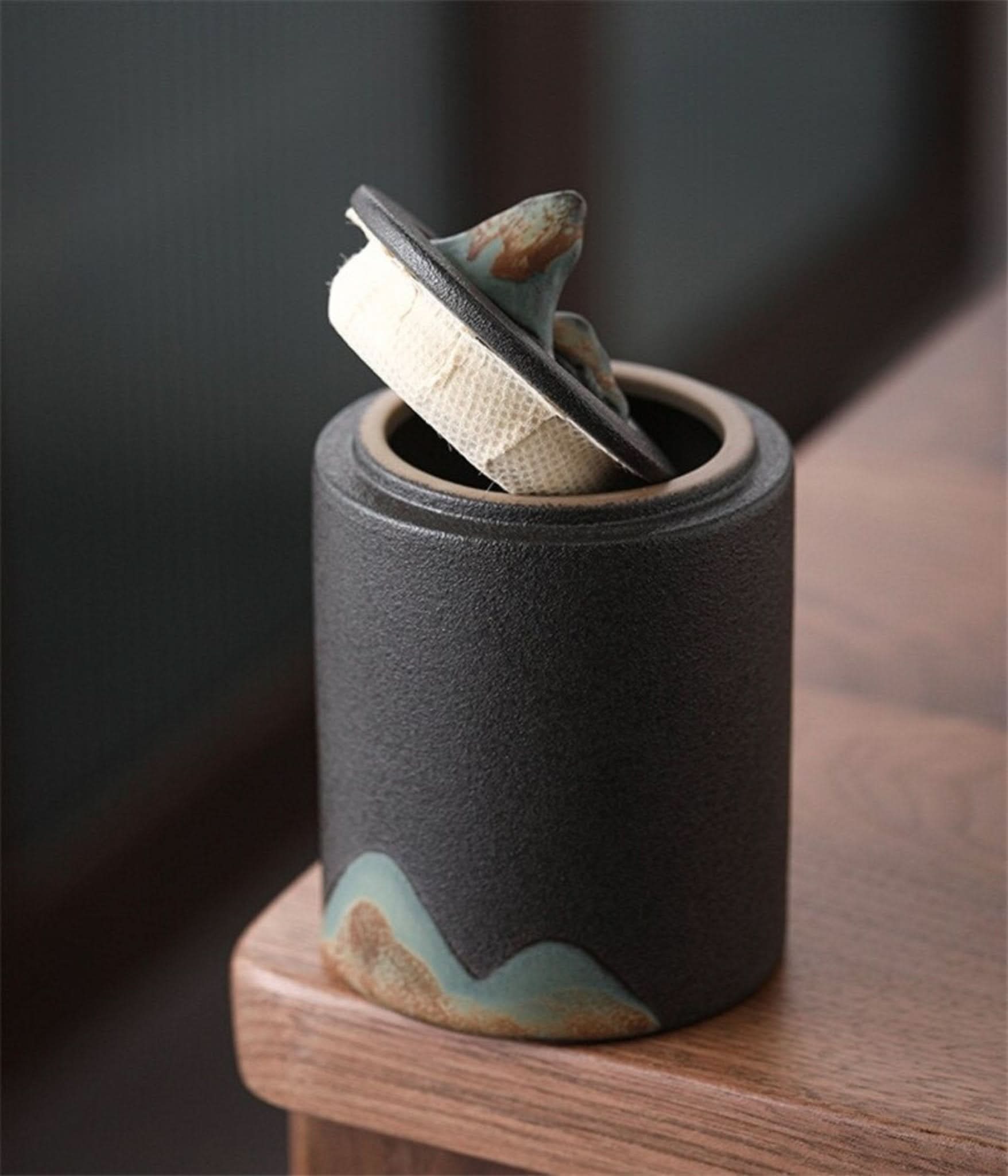 Black matte finish ceramic tea canister with mountain detail, part of home decor collection.