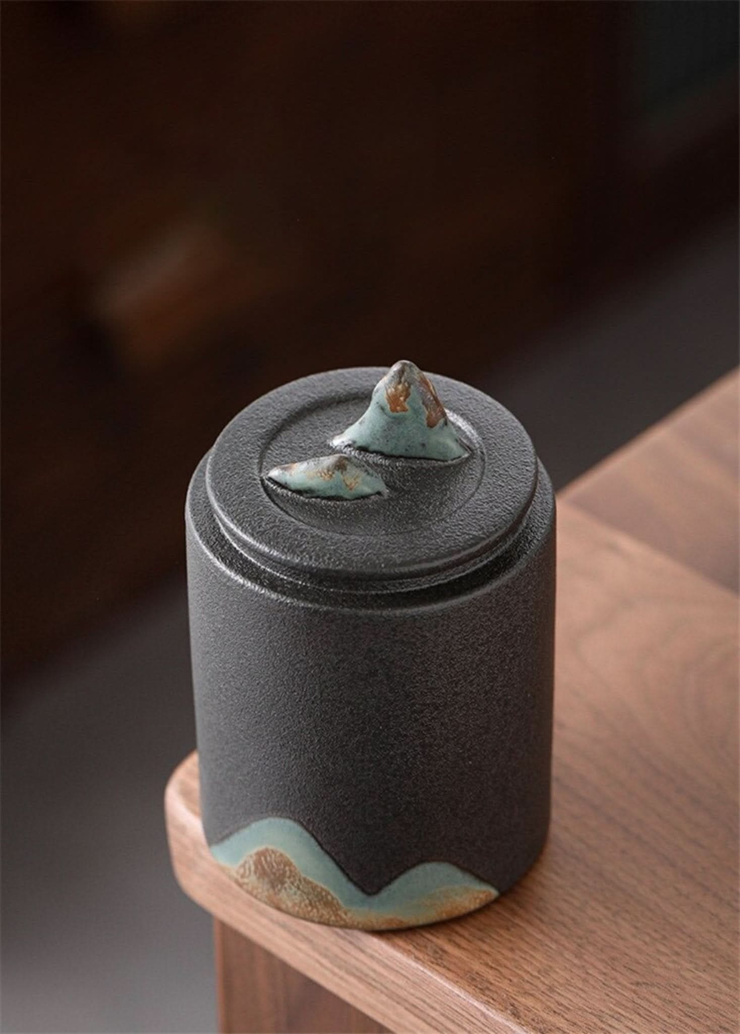 Black matte finish Ceramic Tea Canister with mountain lid on wooden surface.