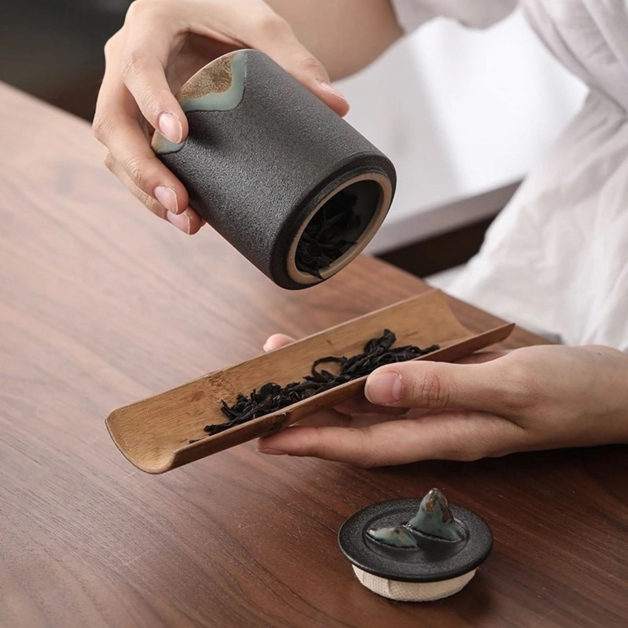 Dark grey ceramic tea canister with matt finish, containing loose tea leaves on wooden surface.