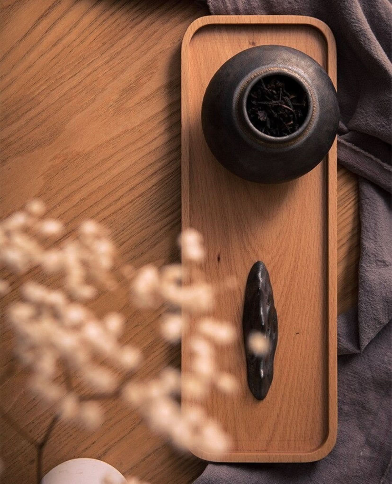 Gray ceramic tea jar with dried tea leaves on a wooden tray, home decor.