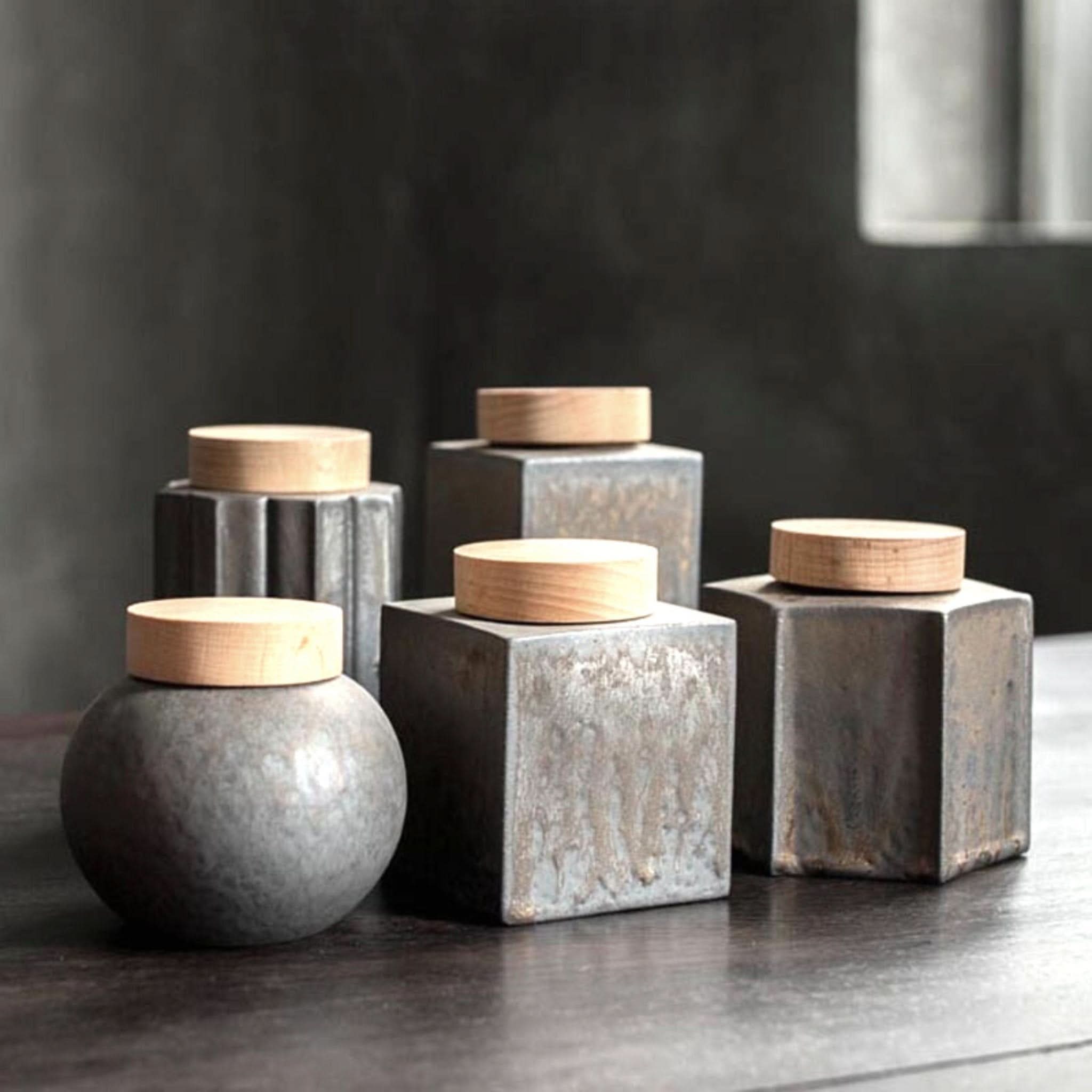 Gray ceramic tea jars with wooden lids on dark surface