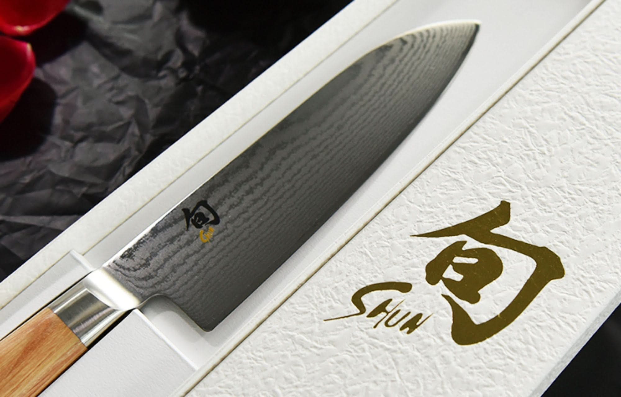 Japanese Damascus Santoku kitchen knife with wooden handle, displayed in a textured white box.