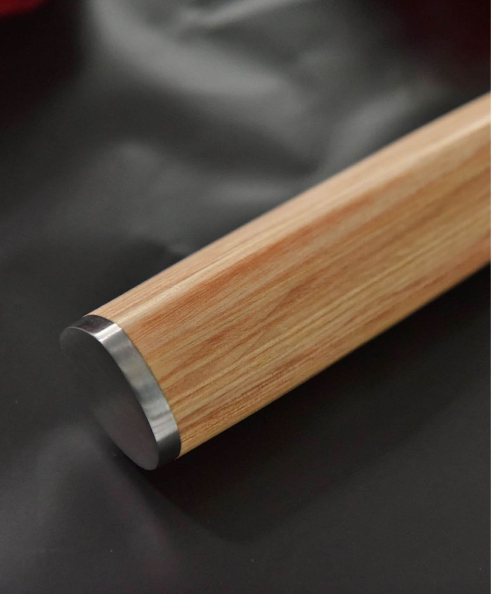 Japanese Santoku knife handle: light wood grain & steel bolster, dark background.