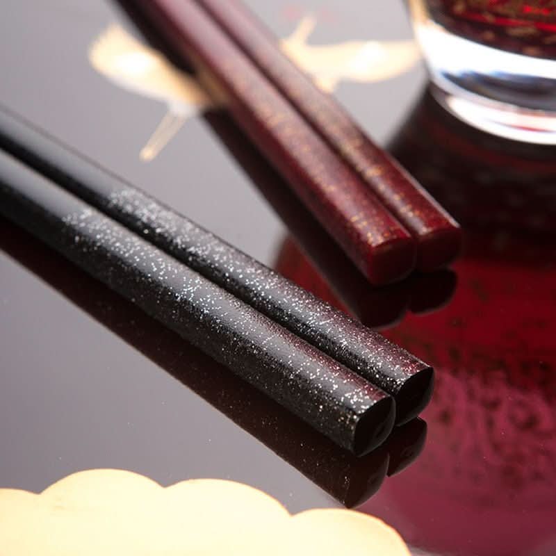Japanese Handmade Wooden Chopsticks in black and burgundy with speckled details on a glossy red surface.