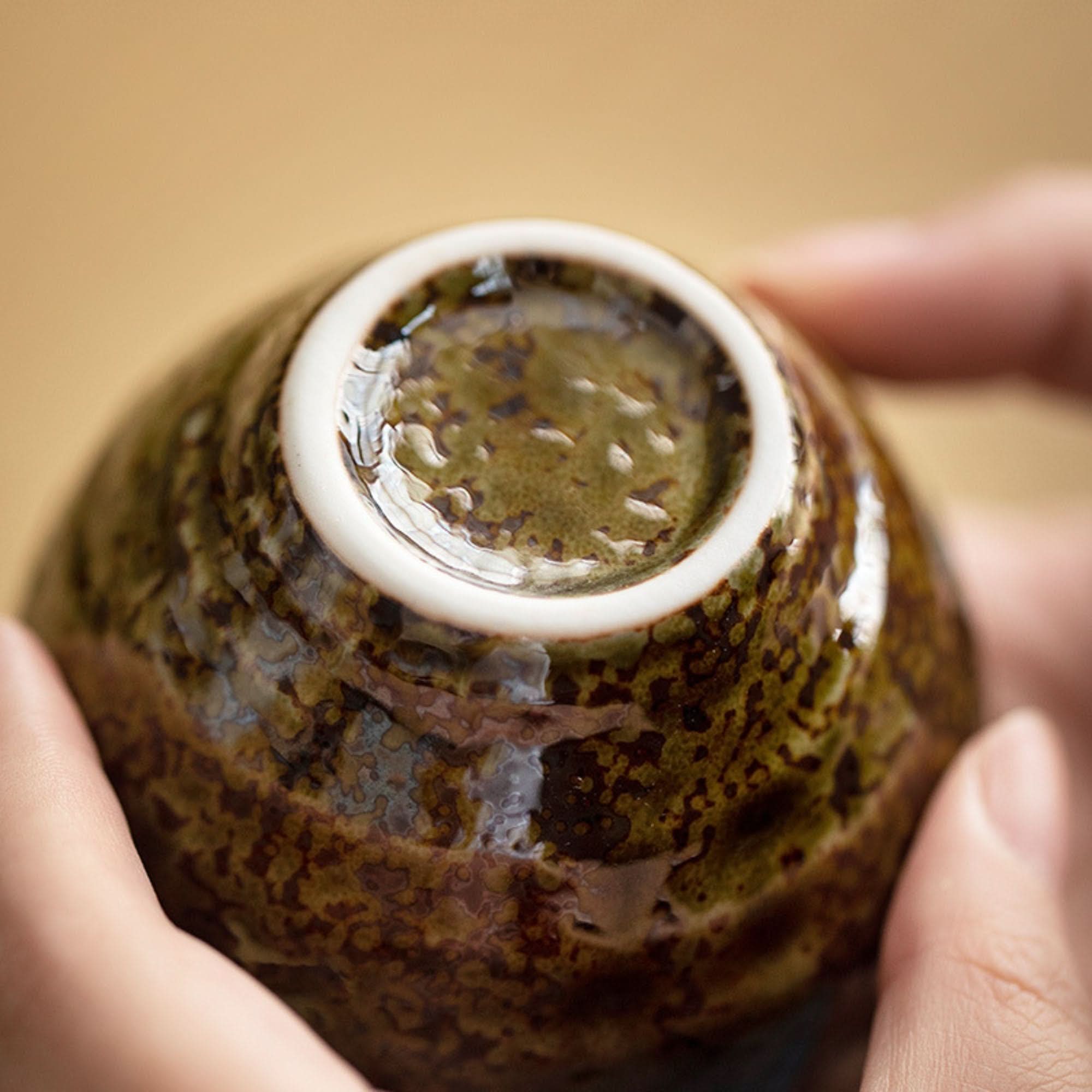 Hands holding a Japanese-imported glazed tea cup set, rustic brown ceramic.