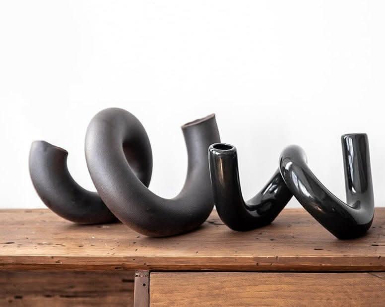 Black ceramic irregular spiral flower vase on wooden table.