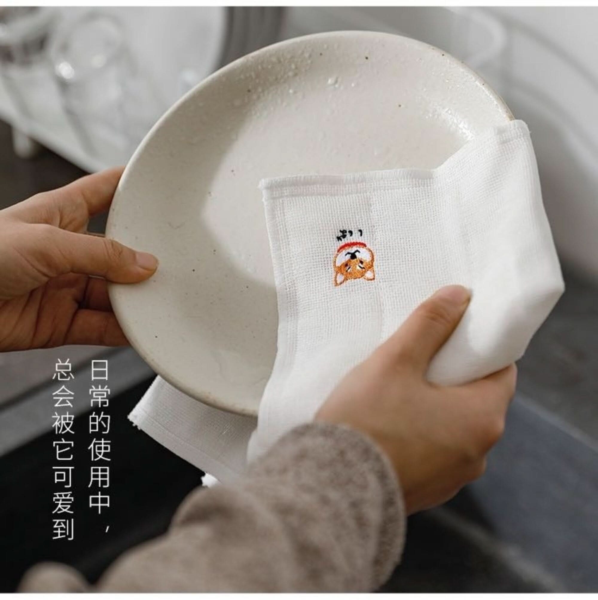 White Japanese linen tea towel with embroidered Shiba Inu, drying a plate.