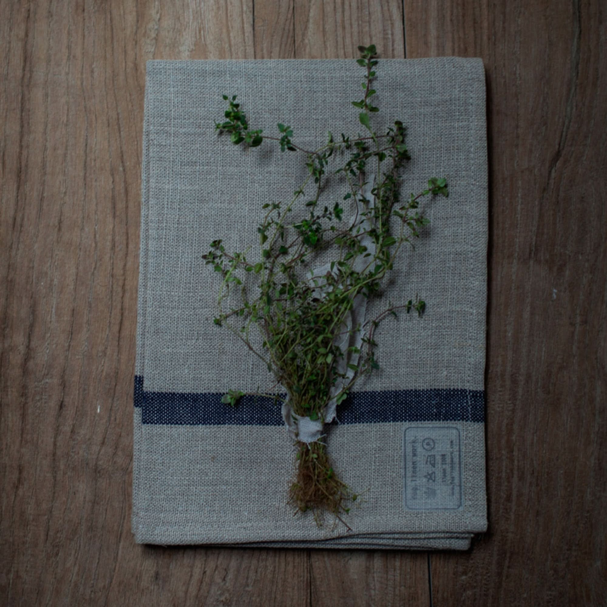 Natural linen Japanese tea towel with navy stripes, adorned with fresh thyme sprigs.