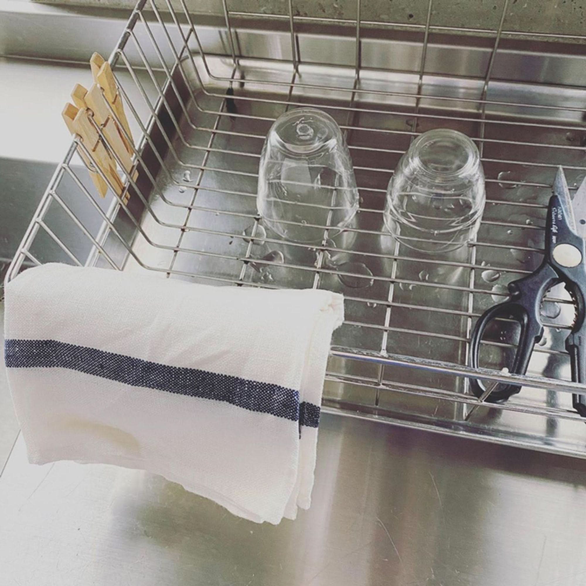 Japanese linen tea towel with blue stripes in a dish rack next to glasses.
