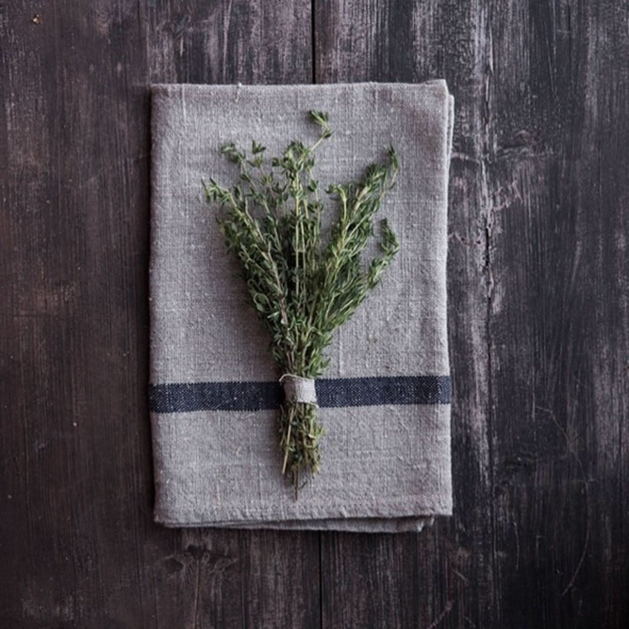 Japanese linen tea towel with a navy stripe and a bundle of thyme on a dark wooden surface.