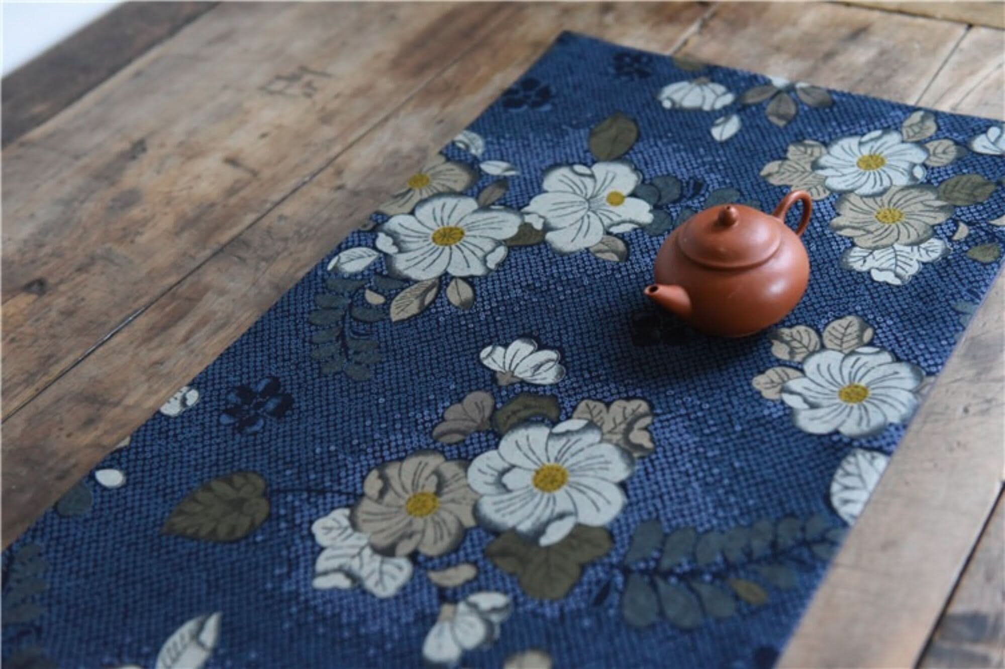 Japanese linen tea towels with floral patterns in blue, on a wooden table with a small teapot.