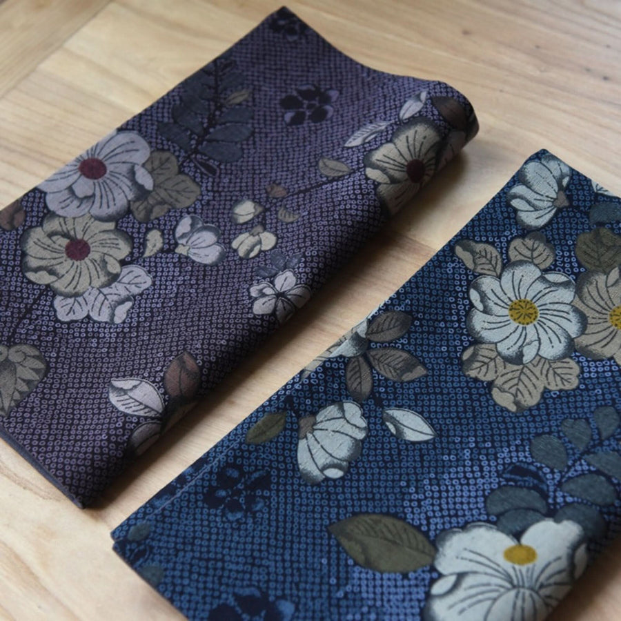 Japanese linen tea towels with floral patterns in blue and purple hues on a wooden surface.