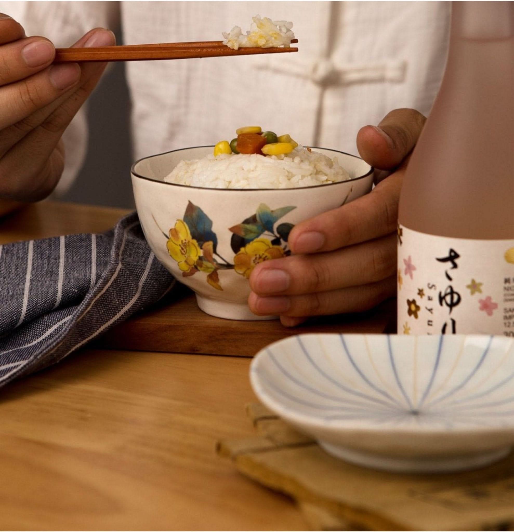 Japanese rice bowl with floral design, being eaten with chopsticks.