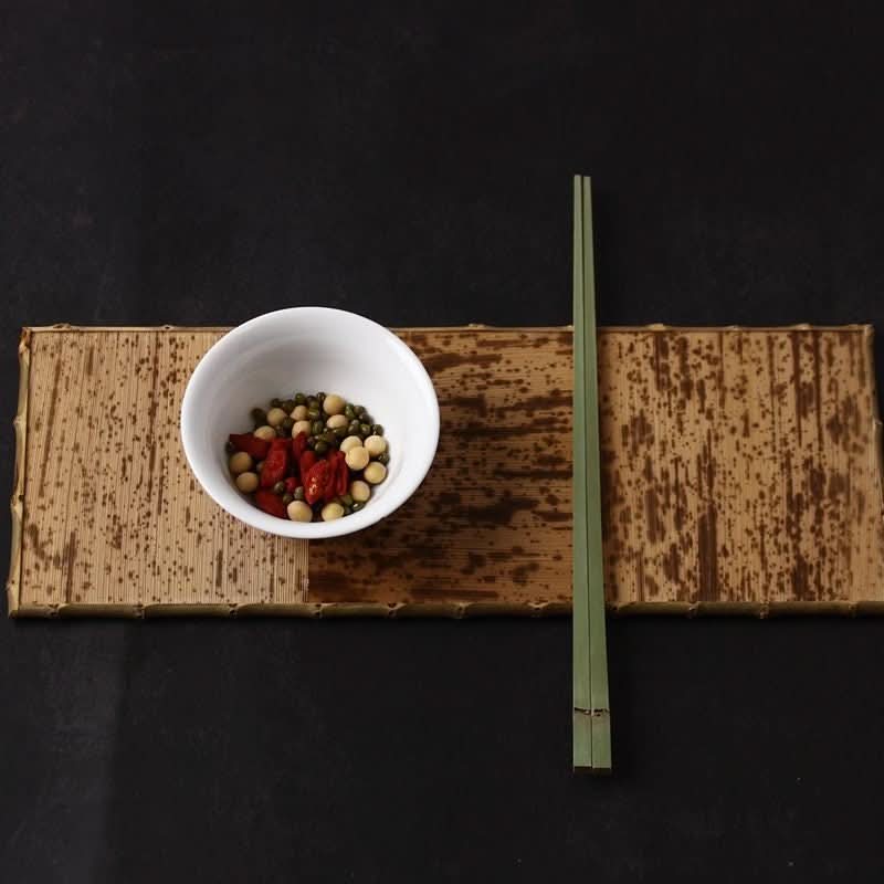 Green Japanese Style Bamboo Shaped Chopsticks on a bamboo mat with a bowl of food.