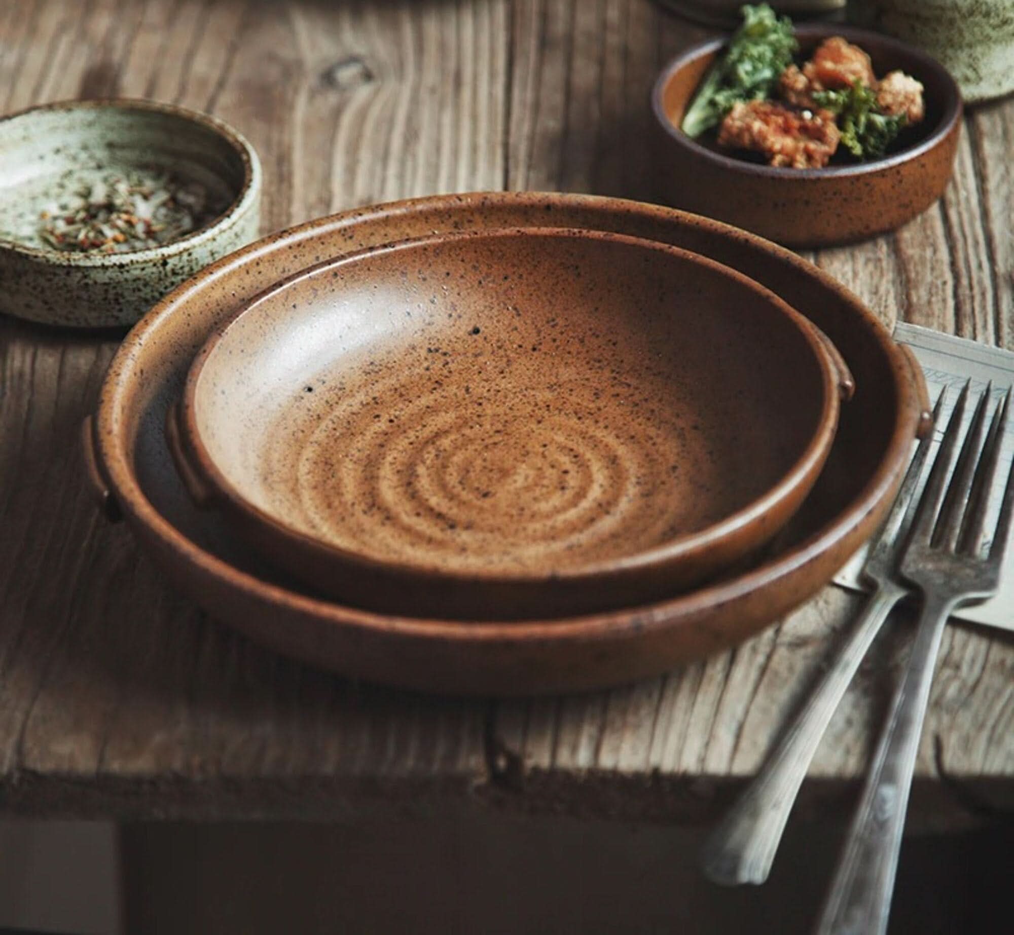 Rustic Dinnerware Brown Speckled ceramic bowls with textured interiors, set on a wooden table with cutlery.
