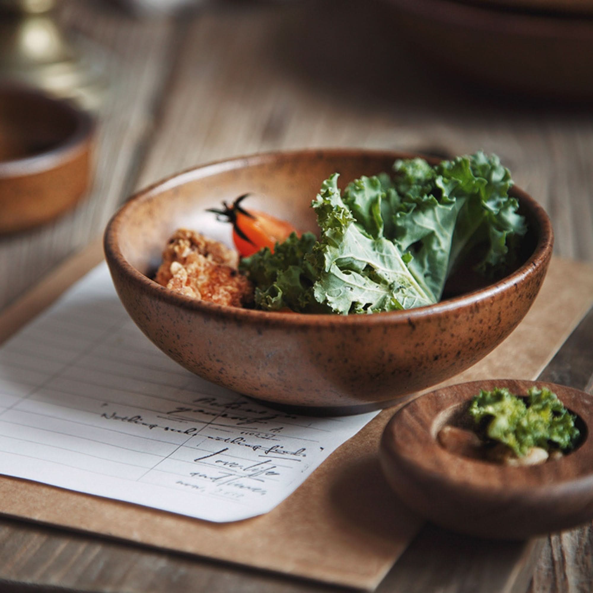Rustic dinnerware brown speckled bowl with food, on paper and wood background.