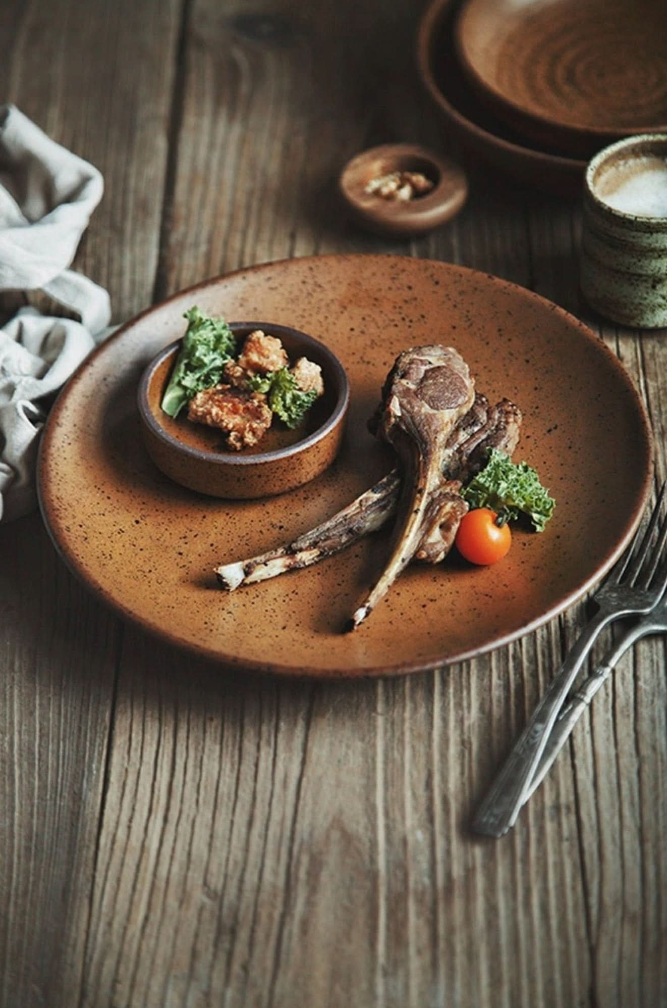 Rustic dinnerware brown speckled plate with lamb chops and a side dish.