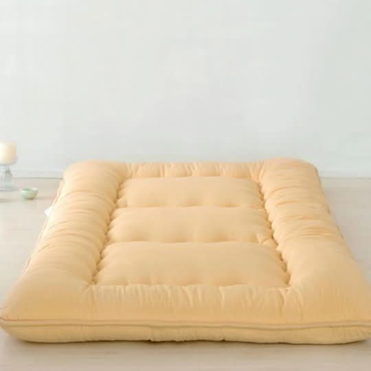 Light yellow Japanese style floor mattress with a soft, quilted texture on a white floor.