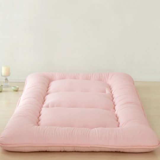 Pink Japanese style floor mattress on a wooden floor, with a candle and small bowls in the background.