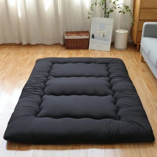 Black Japanese style floor mattress with plush quilting on a wooden floor.