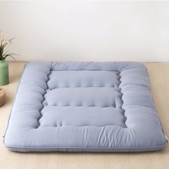 Soft, quilted Japanese style floor mattress in light blue on a wooden floor.