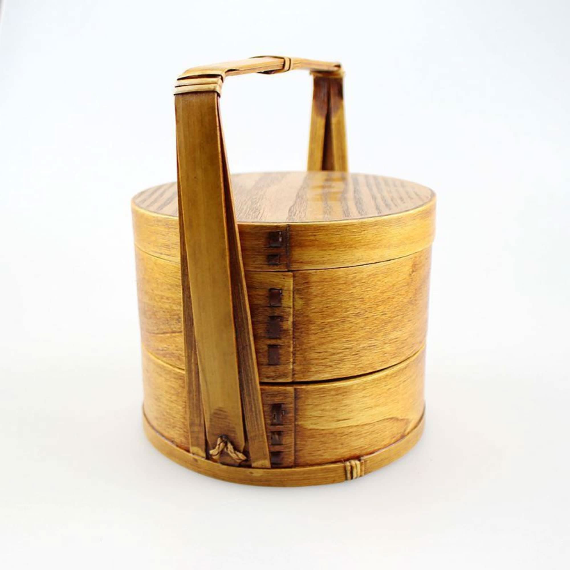 Wooden Japanese lunch box with a handle and three stacked tiers on a white background.